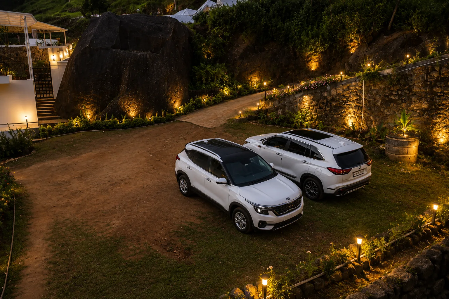 Cars parked on the lit driveway beside the granite boulder at dusk